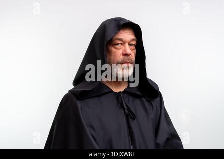 Old male monk in dark monastic clothing isolated in studio on white background Stock Photo