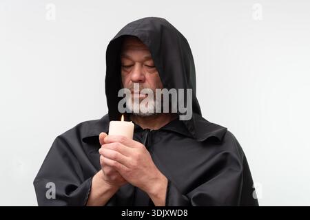 Old male monk in black hood holding candle isolated on white background Stock Photo
