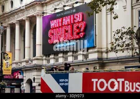 Large neon billboard for the musical 'Why Am I So Single?' on a classic white building with a Tootbus tourist bus passing in the foreground. Stock Photo