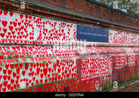 The National Covid Memorial Wall featuring thousands of red heart stickers and handwritten notes of remembrance on a white stone wall. Stock Photo