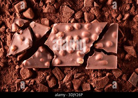 Cracked hazelnut chocolate on cocoa powder and chocolate bars. Hazelnut chocolate on cocoa background. Stock Photo