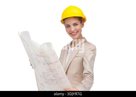 Woman wearing yellow hard hat and beige blazer holding rolled blueprint in white studio. Architect, plan, construction, professional, corporate, portr Stock Photo