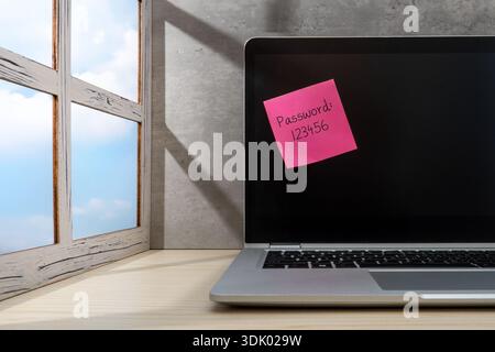 A laptop on a desk and a pink sticky note with a weak password, 123456. Cybersecurity breach, data vulnerability, and digital privacy risks concept. Stock Photo