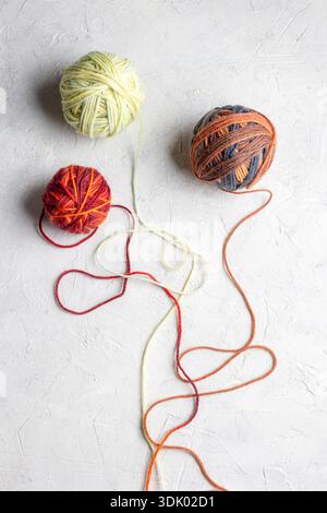 Close‑up photograph of multicolored yarn balls on white teextured background. Depth of field highlights the fibers, colors and tactile quality of the Stock Photo