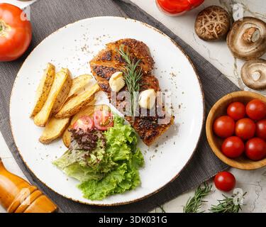 Delicious grilled salmon steak served with roasted potatoes, fresh salad, and condiments on a white ceramic plate, perfect for a healthy meal. Stock Photo