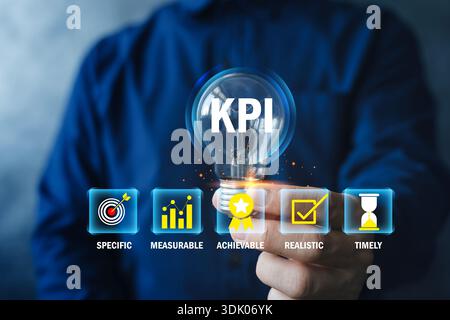 Businessman holding KPI lightbulb with SMART goal icons, showing key performance indicators for planning, tracking progress, and improving business re Stock Photo