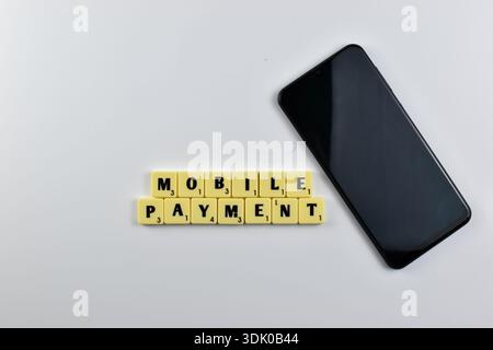 Scrabble tiles spell Mobile Payment beside a smartphone, symbolizing digital transactions via mobile devices in modern financial systems. Stock Photo