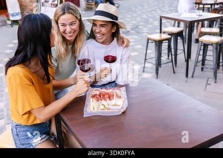 Three young women friends enjoying wine at outdoor cafe Stock Photo