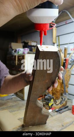 Male hands hold a bottle of glue and a wooden piece with holes and apply adhesive material to the cut for gluing wooden parts, joining parts Stock Photo