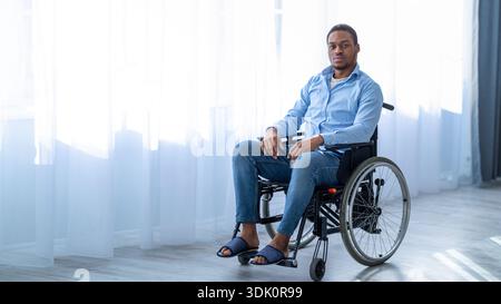 Young Black Man Using a Wheelchair Sitting Indoors Near a Window With Natural Light Stock Photo