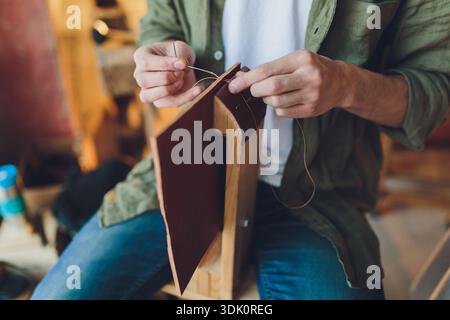Handcrafted leather journal. Focused image of homemade leather book being handcrafted. Intimate view of skilled craftsman sewing waxed thread onto Stock Photo