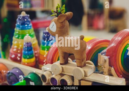 Crafted wooden stag surrounded by playful colorful toy accessories for display. Artisan carved deer amidst multicolored wooden train and stacking toys Stock Photo