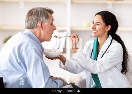 Doctor Feeding an Older Man in a Bright Room During a Medical Consultation Session Stock Photo