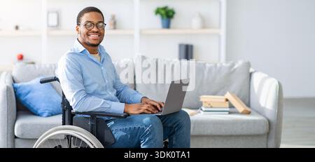 Young Black Man Using a Wheelchair Works on a Laptop at Home Stock Photo