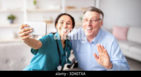 Caregiver and Elderly Man Enjoying a Moment While Taking a Selfie in a Cozy Living Room Stock Photo