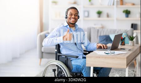 Young Black Man Using a Wheelchair Smiles and Works on a Laptop at Home Office Stock Photo