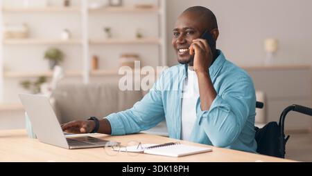 Man Using a Wheelchair Smiles While Talking on the Phone and Working on a Laptop in a Modern Office Stock Photo