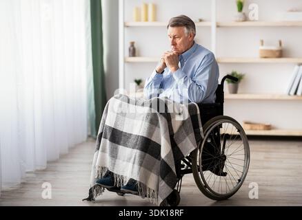 Older Man in a Wheelchair Sits Thoughtfully With a Blanket in a Cozy Living Space Stock Photo