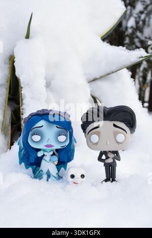 Funko Pop action figures of Emily and Victor with Scraps from gothic animated dark fantasy film Corpse Bride. Green plant under white fluffy snow. Stock Photo