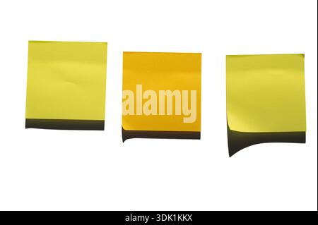 Three yellow sticky notes are arranged side by side against a white surface. The left note is a darker shade, while the two on the right are lighter. Stock Photo