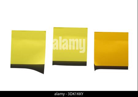 Three yellow sticky notes are arranged side by side against a white surface. The left note is a darker shade, while the two on the right are lighter. Stock Photo