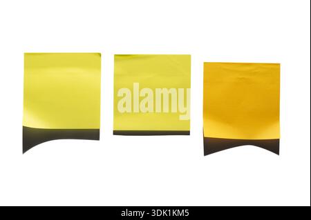 Three yellow sticky notes are arranged side by side against a white surface. The left note is a darker shade, while the two on the right are lighter. Stock Photo