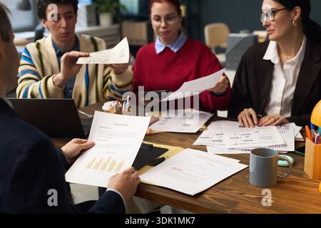 Group of young adult and middle aged multiethnic men and women discussing financial charts and business documents at table, collaborating on project, using laptop and digital tablet Stock Photo