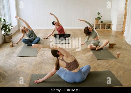 Group of Young Adult Women Practicing Seated Yoga Stretching Together Stock Photo