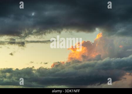Single yellow cloud illuminated by sunset light against dark stormy sky. Dramatic atmospheric sky background, contrast of light and darkness, weather, Stock Photo