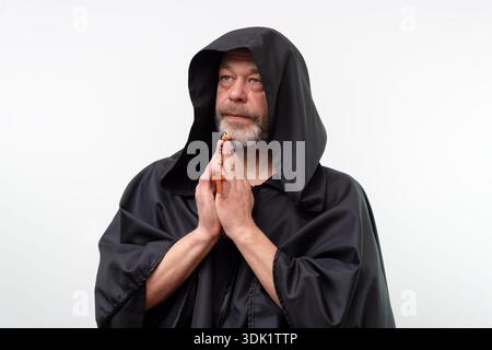 Elderly monk in black robe with folded hands holding rosary Stock Photo