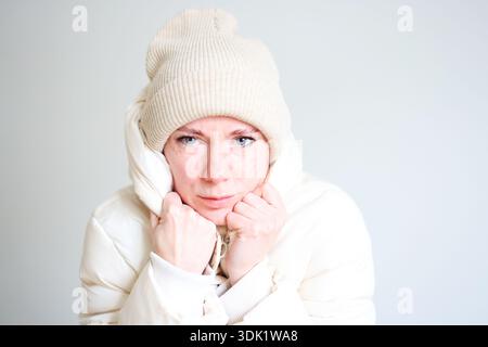 Young woman in white winter jacket with hood posing against clean light background Stock Photo