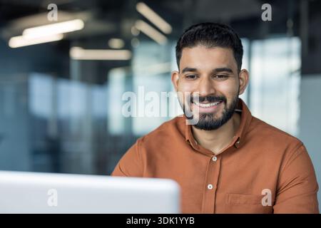 Smiling man enjoying remote work, finding success and embracing a modern digital nomad lifestyle while working on a laptop in a vibrant office environ Stock Photo