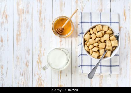 tasty corn pillows in a ceramic bowl with milk and honey on a white wooden table, top view. healthy breakfast with corn pillows. Stock Photo