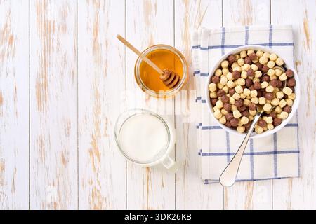 corn balls and chocolate corn balls in a ceramic bowl with milk and honey on a white wooden table, top view. Stock Photo