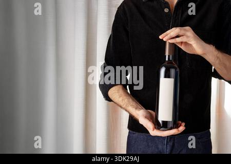 Guy in black shirt holding a wine bottle with a neutral label. Light background for mockup. Stock Photo