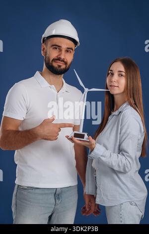 Male electrician engineer is with woman that holds toy wind turbine. Stock Photo