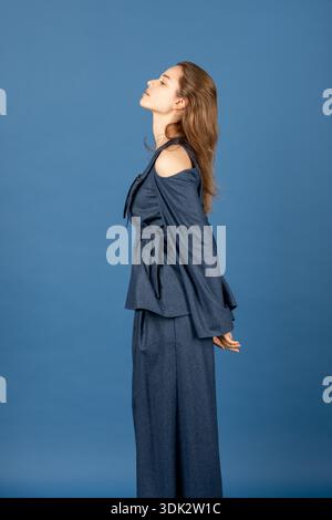 Woman standing looking up with closed eyes on blue background Stock Photo