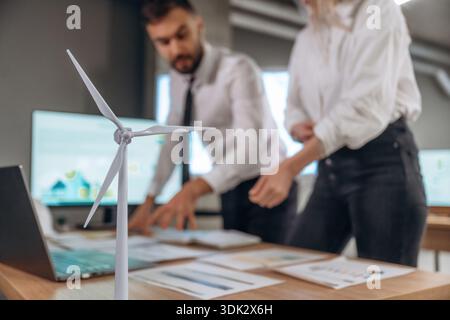 Blurred, focused on wind turbine model. Two employees are working in company. Stock Photo