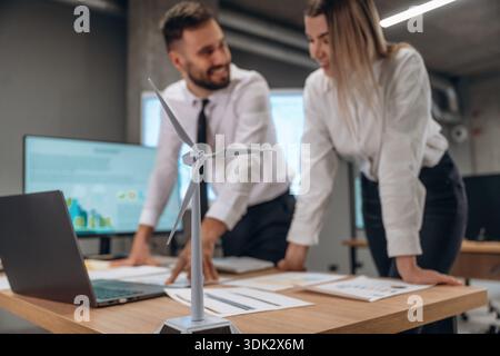 Blurred, focused on wind turbine model. Two employees are working in company. Stock Photo