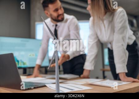 Blurred, focused on wind turbine model. Two employees are working in company. Stock Photo
