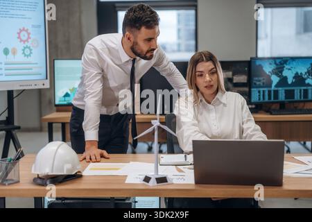 Laptop and documents on table. Two employees are working in wind turbine company. Stock Photo