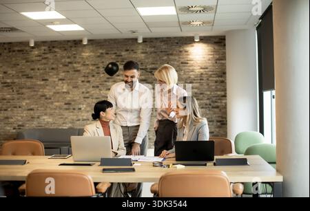 Four professionals engage in a lively discussion around a table in a contemporary office. Laptops and documents are present as they share ideas and st Stock Photo