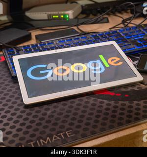 Tablet displaying Google logo on modern workspace with backlit keyboard and network equipment, representing search engine technology, internet connect Stock Photo