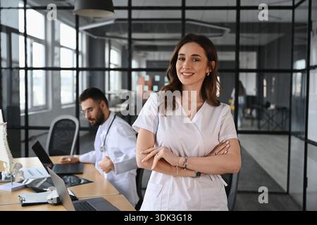 Woman is standing with arms crossed. Two doctors are in the office. Stock Photo