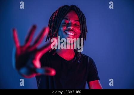 Smiling, positive facial expression. African American guy is studio with neon lighting. Stock Photo