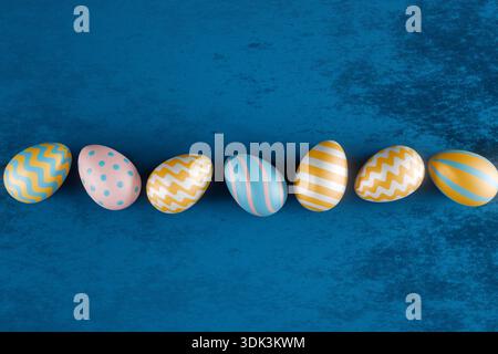 Seven decorated Easter eggs in pastel colors lined up on a blue surface for Easter celebration. 3d rendering Stock Photo