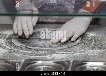 Close up of pizzaiolo hands stretching raw dough base on stone counter with flour during cooking process. Stock Photo