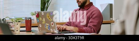 Header of Young Adult Man Working Remotely on Laptop in Modern Office Setting Stock Photo