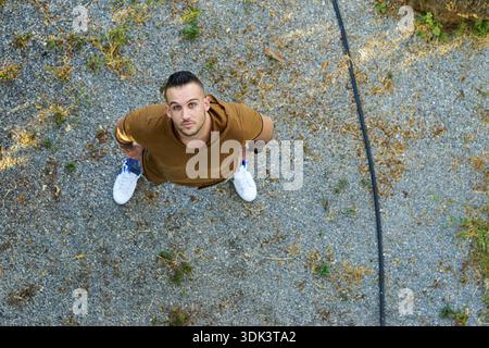 Overhead shot of a confident Greek man looking upwards while standing on gravel in a casual outfit, gardening pipe, garden hose, hosepipe, drought, dr Stock Photo