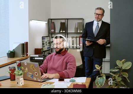 Young Adult Man Using Laptop While Middle Aged Man Observing Stock Photo